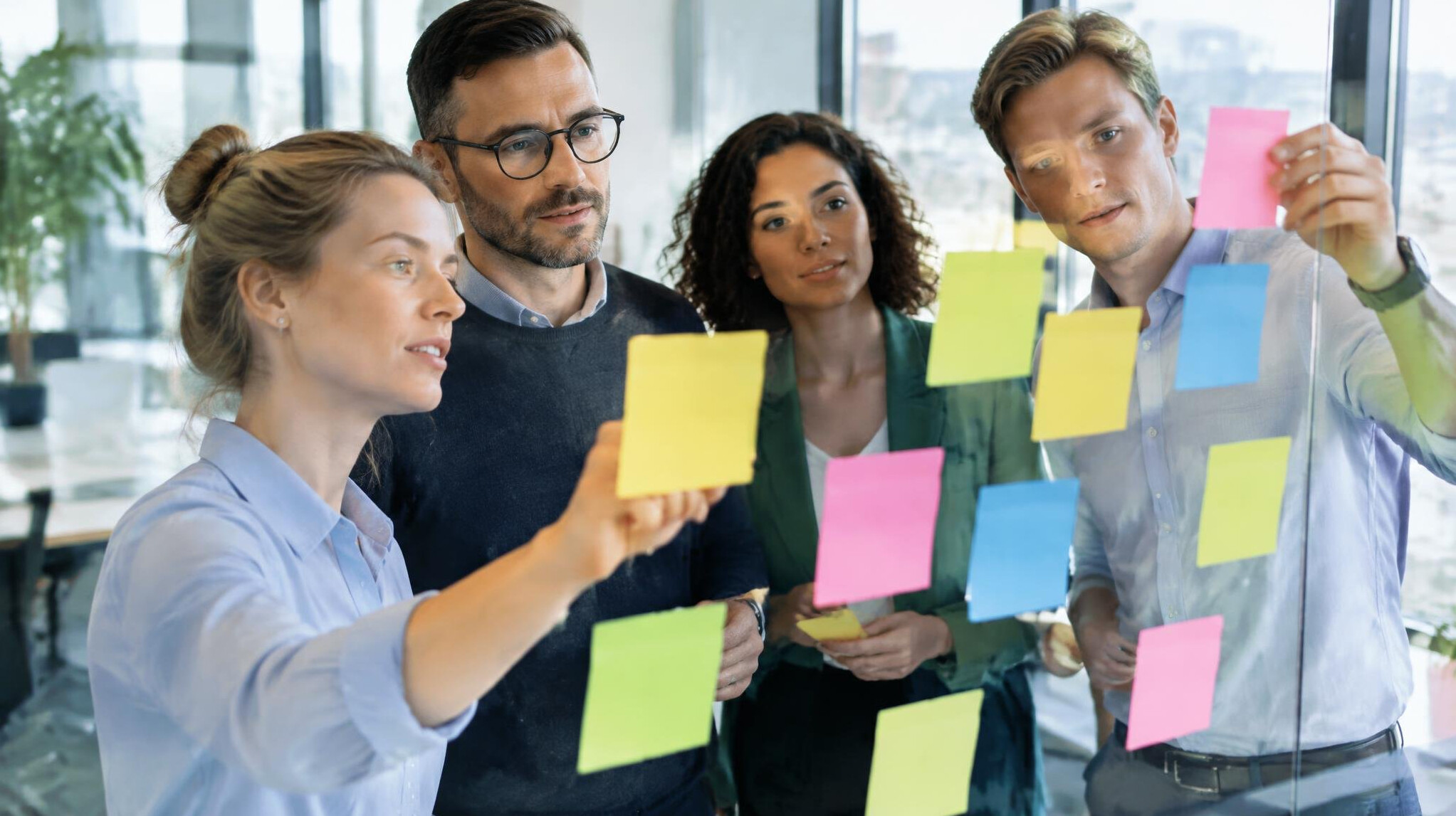 Colleagues collaborating with sticky notes on a glass wall